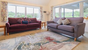 A living room with two sofas, a chandelier, and a view of the countryside through large windows.