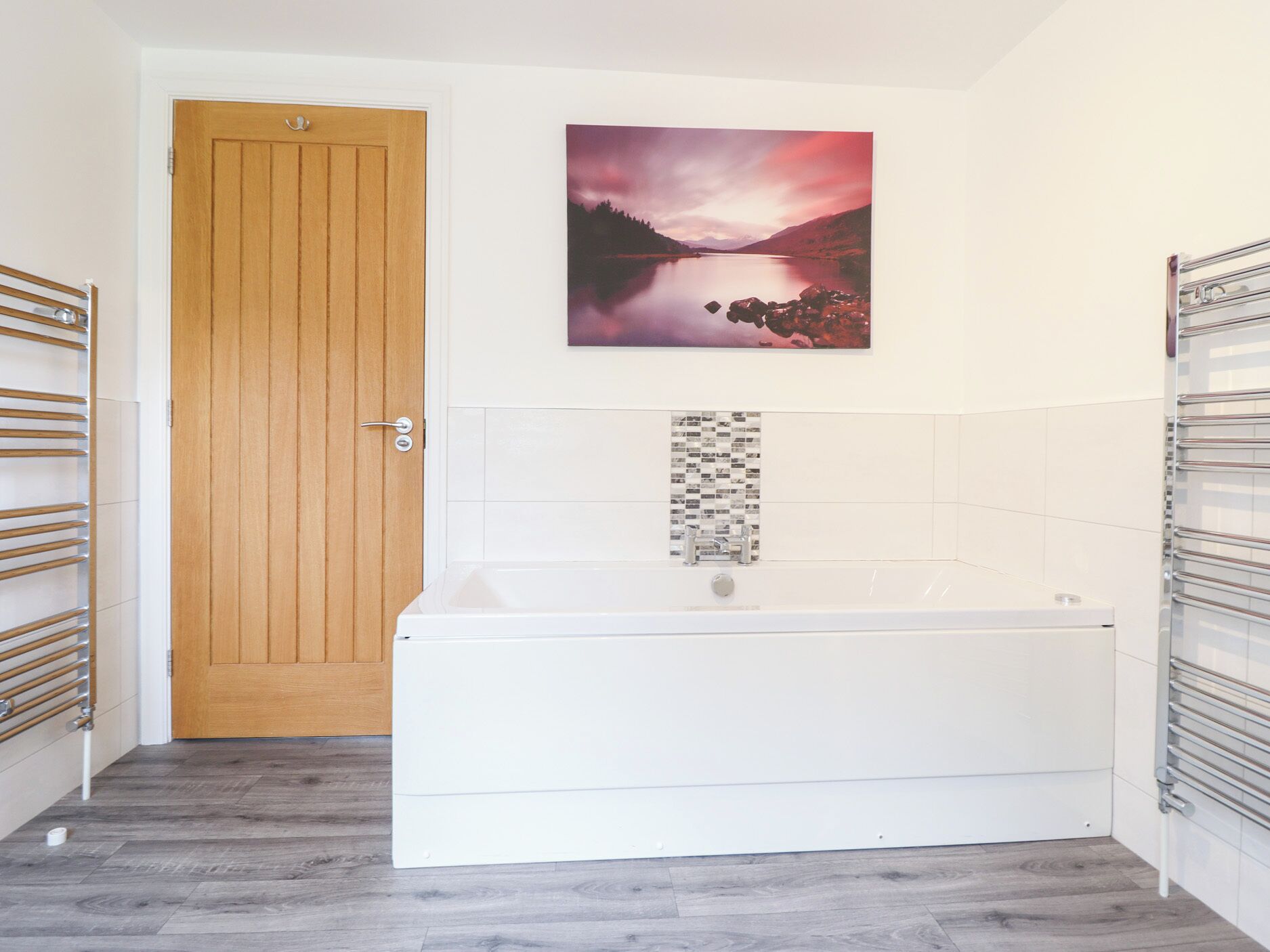 A bathroom with a wooden door, a white bathtub, and a wall-mounted towel rack.
