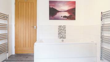 A bathroom with a wooden door, a white bathtub, and a wall-mounted towel rack.
