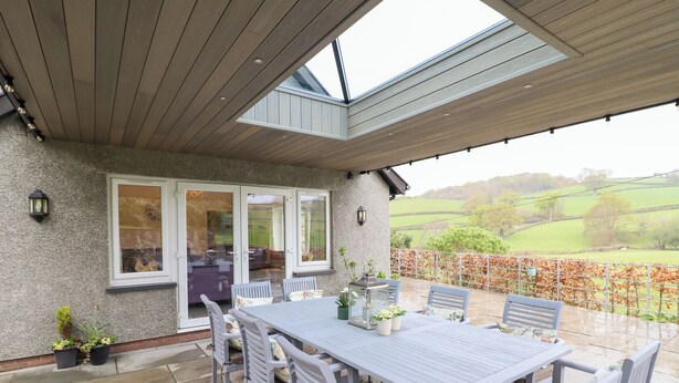 An outdoor patio with a table and chairs, a stone wall, and a view of the countryside.