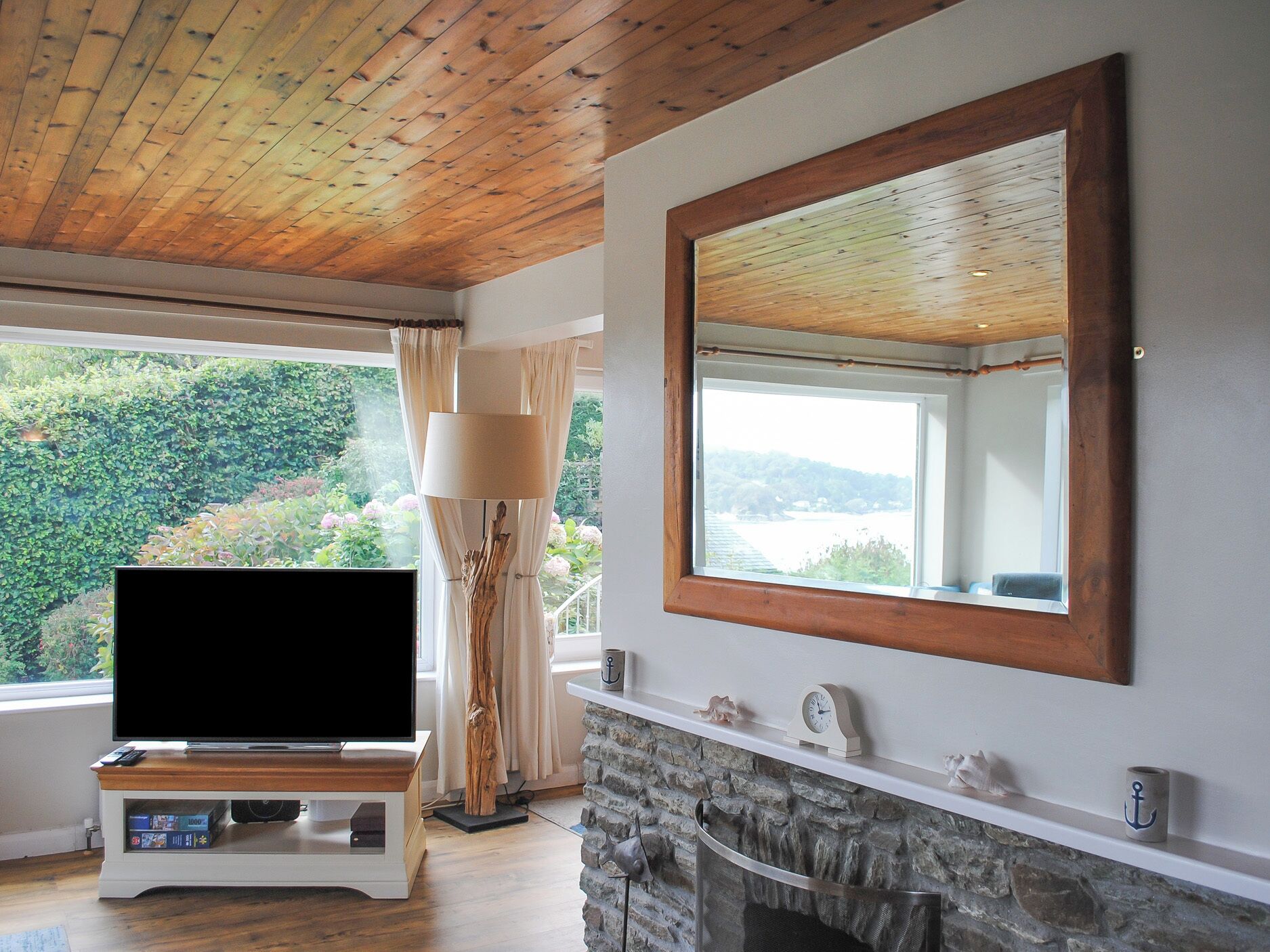 Una sala de estar con televisión, chimenea y ventanas amplias que dan a un bosque.