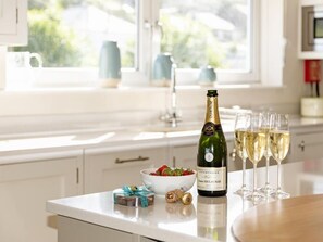 A kitchen counter with a bottle of champagne, glasses, a bowl of fruit, and a gift box. - Quayside (Salcombe)