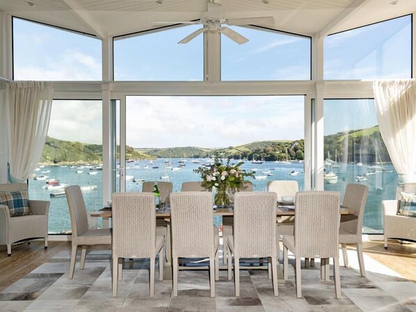 A dining area with a view of boats on the water, large windows, and wicker chairs. - Quayside (Salcombe)