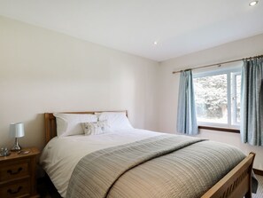Une chambre à coucher avec un lit, une tête de lit en bois, une table de chevet avec une lampe et une fenêtre avec des rideaux.