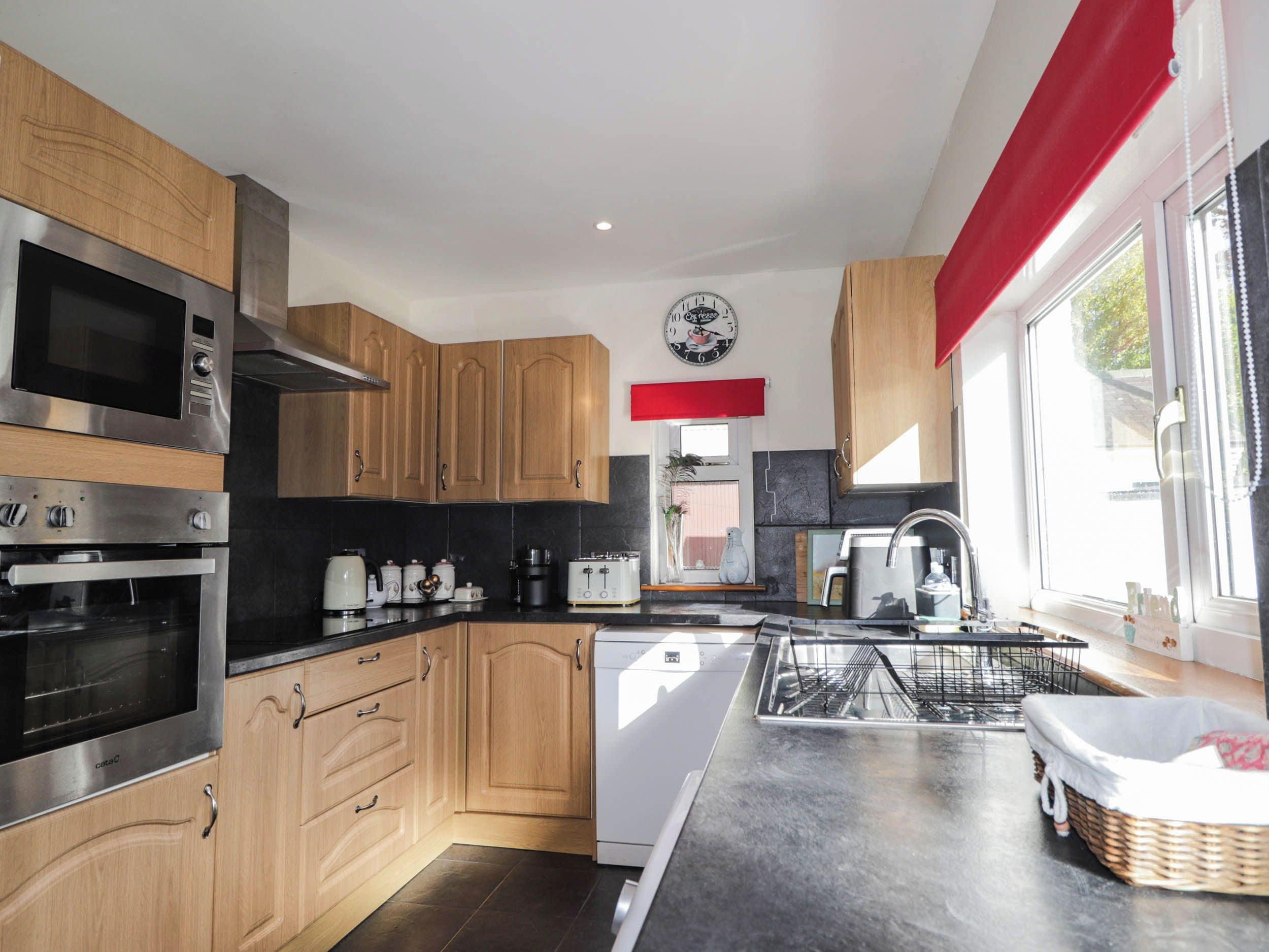 A modern kitchen with stainless steel appliances, wooden cabinets, a dishwasher, and a large window with a red curtain.