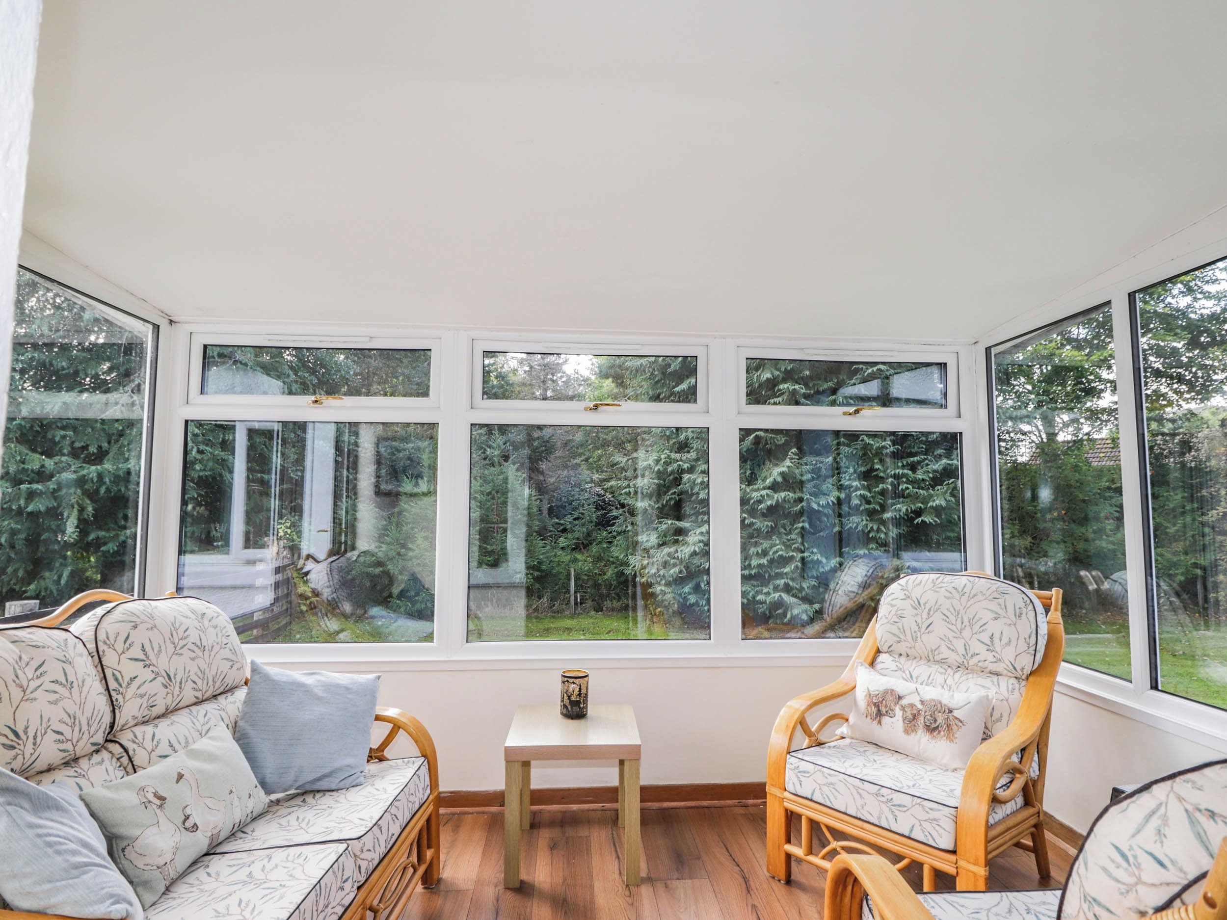 A room with a large window, two wicker chairs, a small table, and a sofa with floral upholstery.