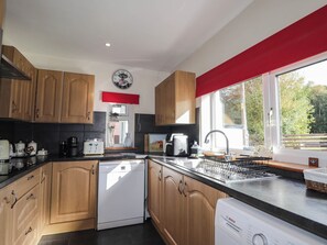 A modern kitchen with wooden cabinets, a Bosch dishwasher, a coffee machine, and a window with a red blind. - St. Aethans (Invershin)