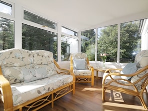 Une pièce lumineuse, avec un canapé et deux fauteuils, de grandes fenêtres et un plancher en bois.
