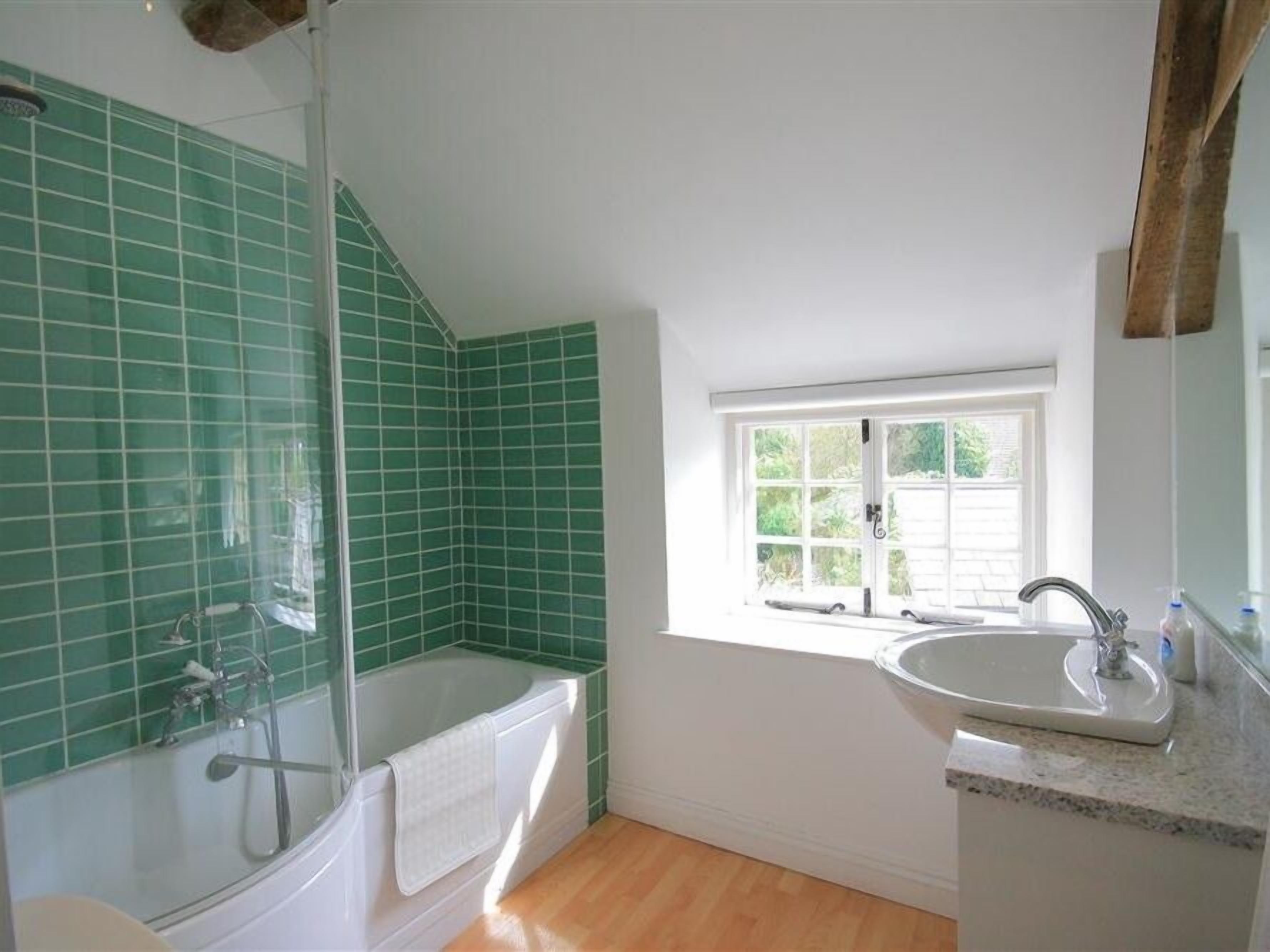 A bathroom with a bathtub, shower, and sink. There is a window providing natural light.