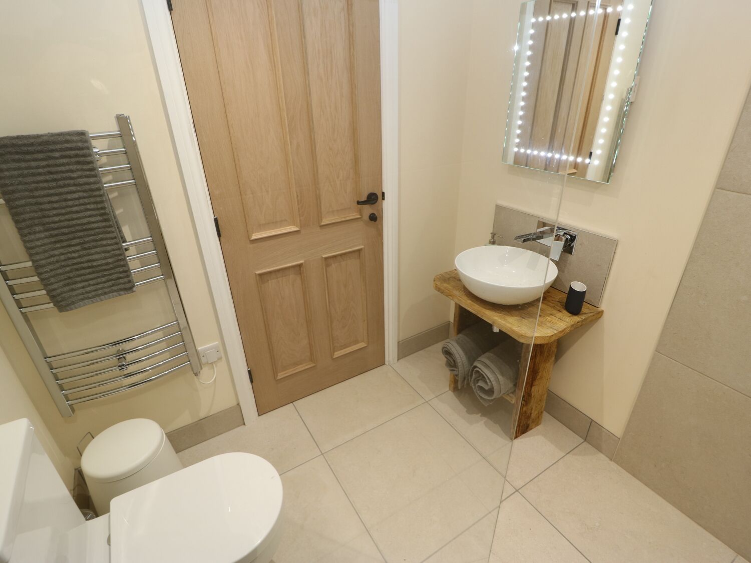 A bathroom with a wooden door, a white sink with a mirror above it, and a towel rack with a towel.
