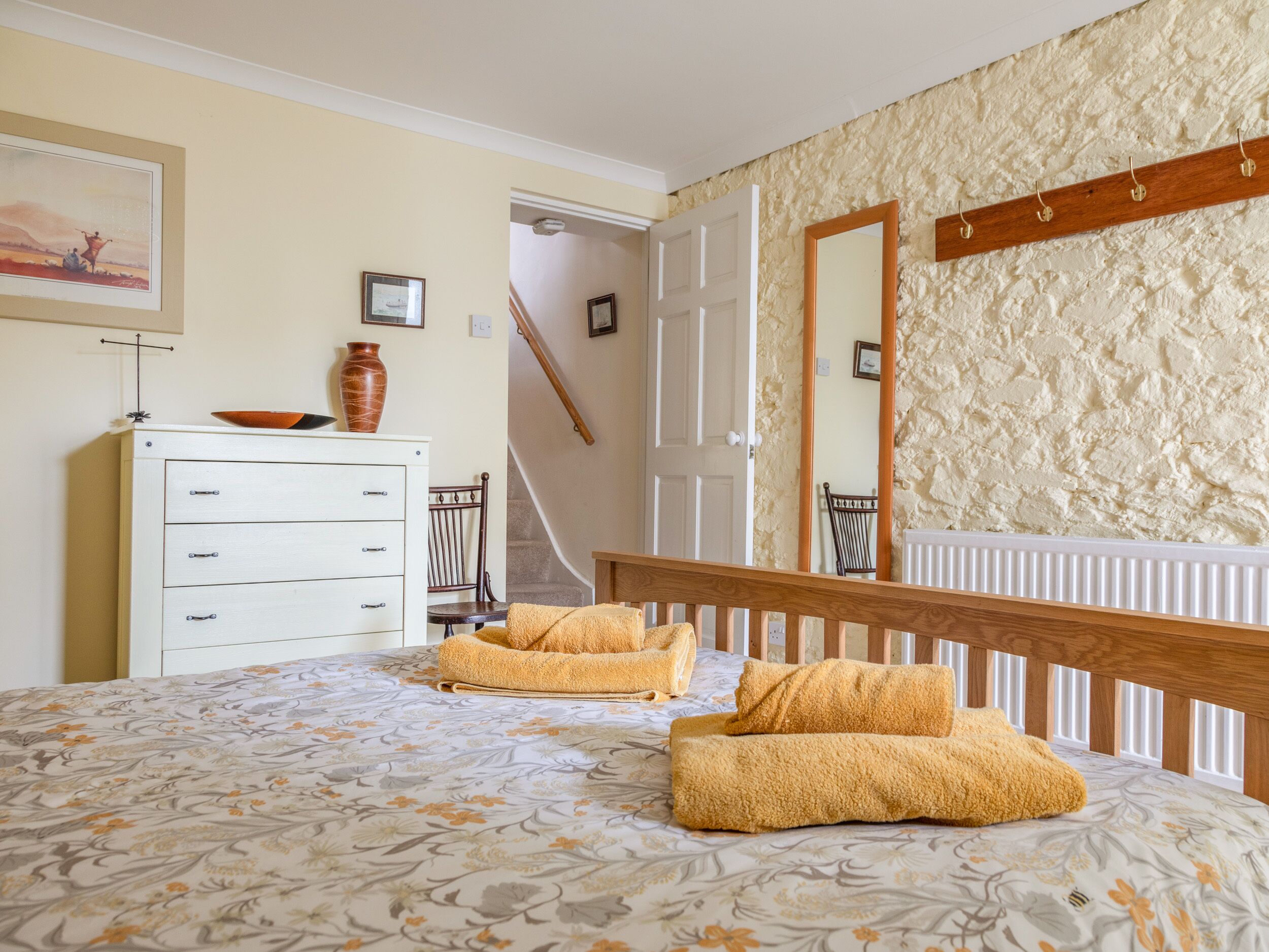 A bedroom with a bed, a dresser, a mirror, and a staircase.