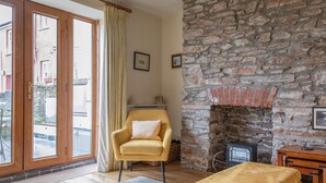 Een gezellige woonkamer met een stenen openhaard, een gele fauteuil en een groot raam met gordijnen.