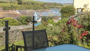 Een balkon met een tafel en stoelen met uitzicht op een haven met boten, een stenen muur en begroeiing.