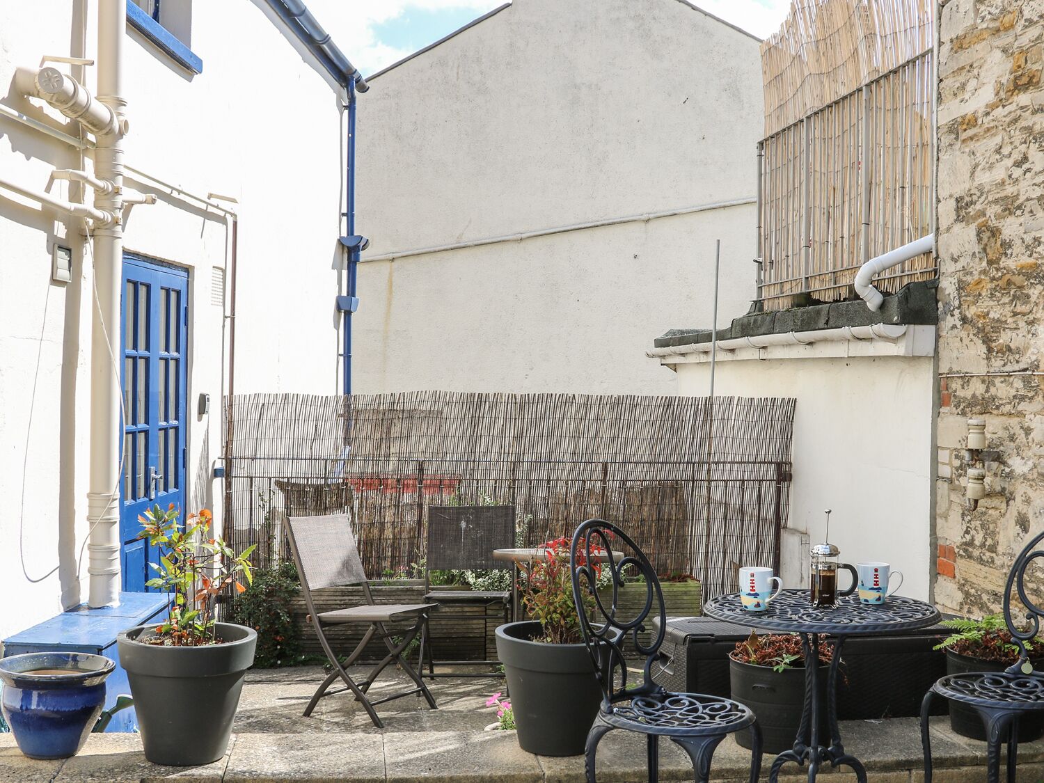 A courtyard with a blue door, outdoor seating, and potted plants.