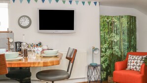 En matplats med ett träbord, stolar, en tv och en gardin med skogsmotiv.
