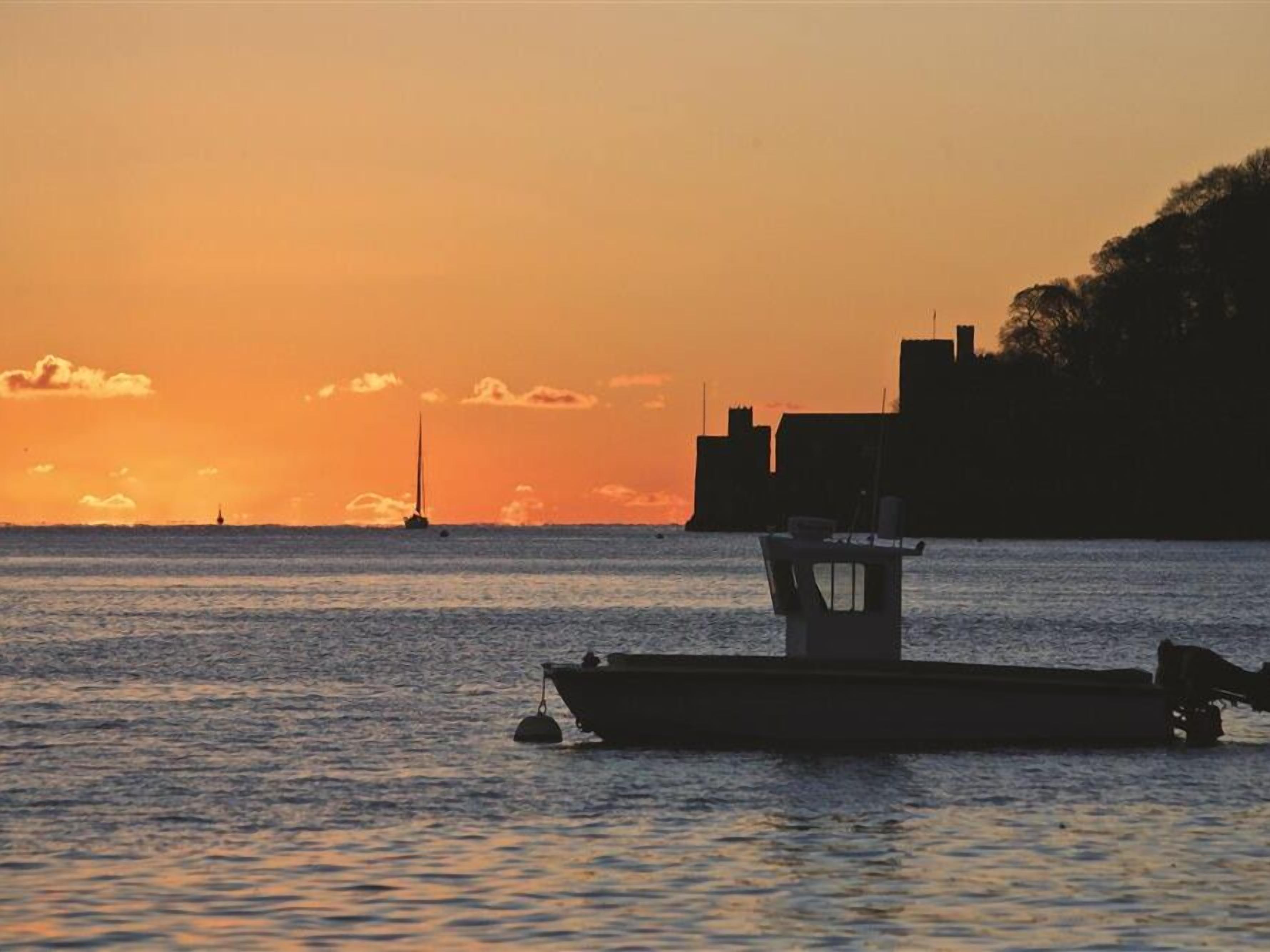 Een boot afgemeerd langs een oever, met een zonsondergang op de achtergrond.