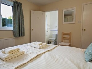 Een slaapkamer met een bed, een stoel, een raam met gordijnen en een deur naar een badkamer.
