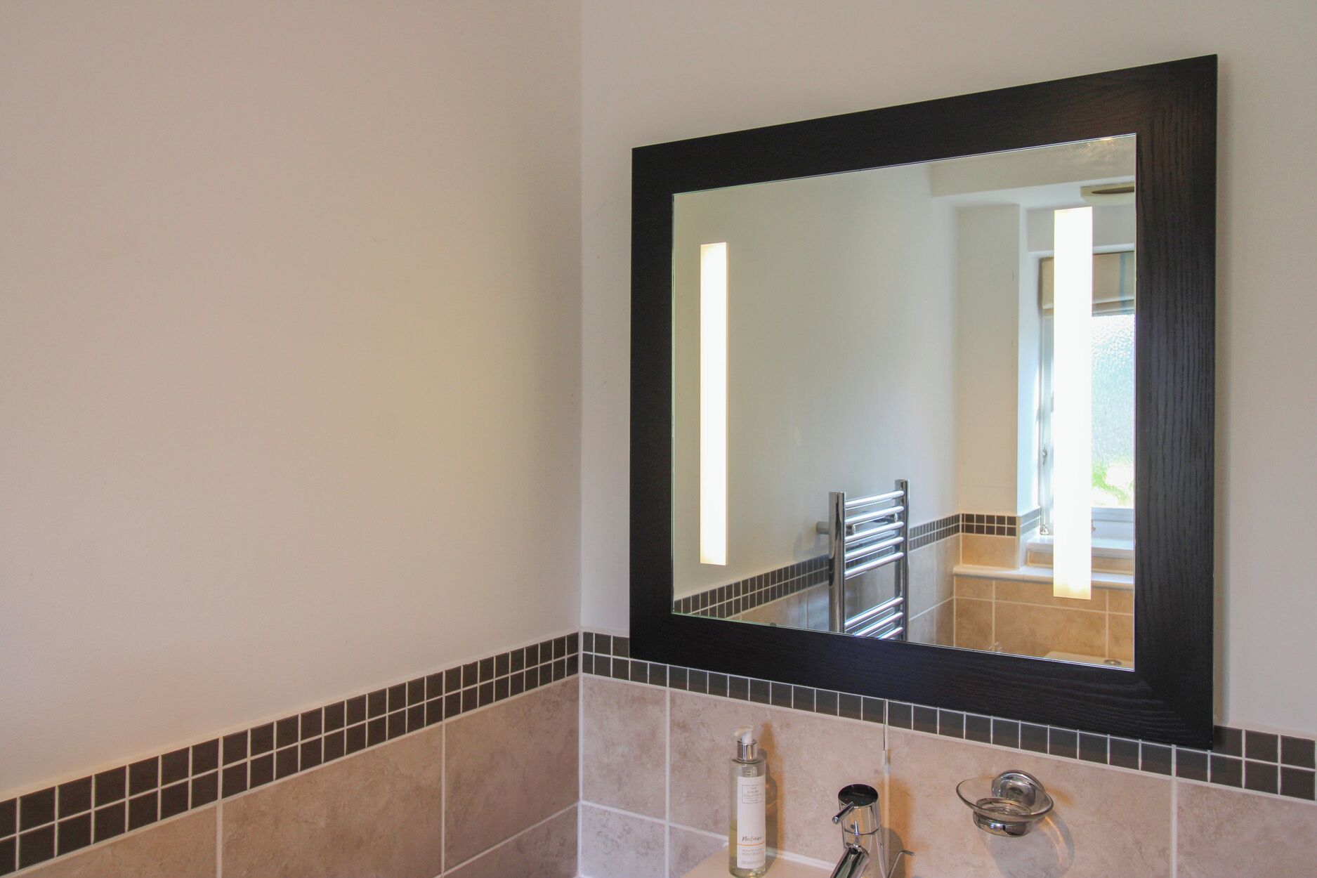 A bathroom with a large mirror, a towel rack, and a bottle of lotion.