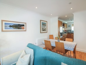 A living room with a sofa, a dining table with chairs, and a kitchen in the background.