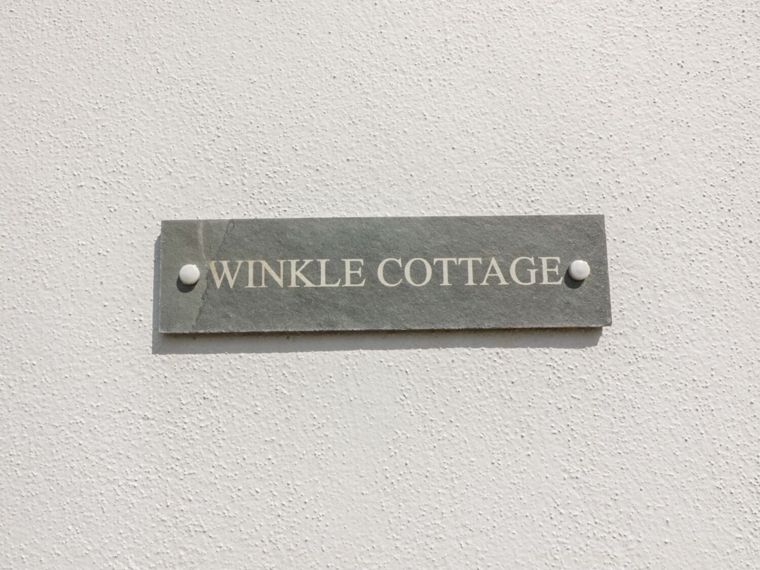 A sign on a wall that reads "Winkle Cottage."