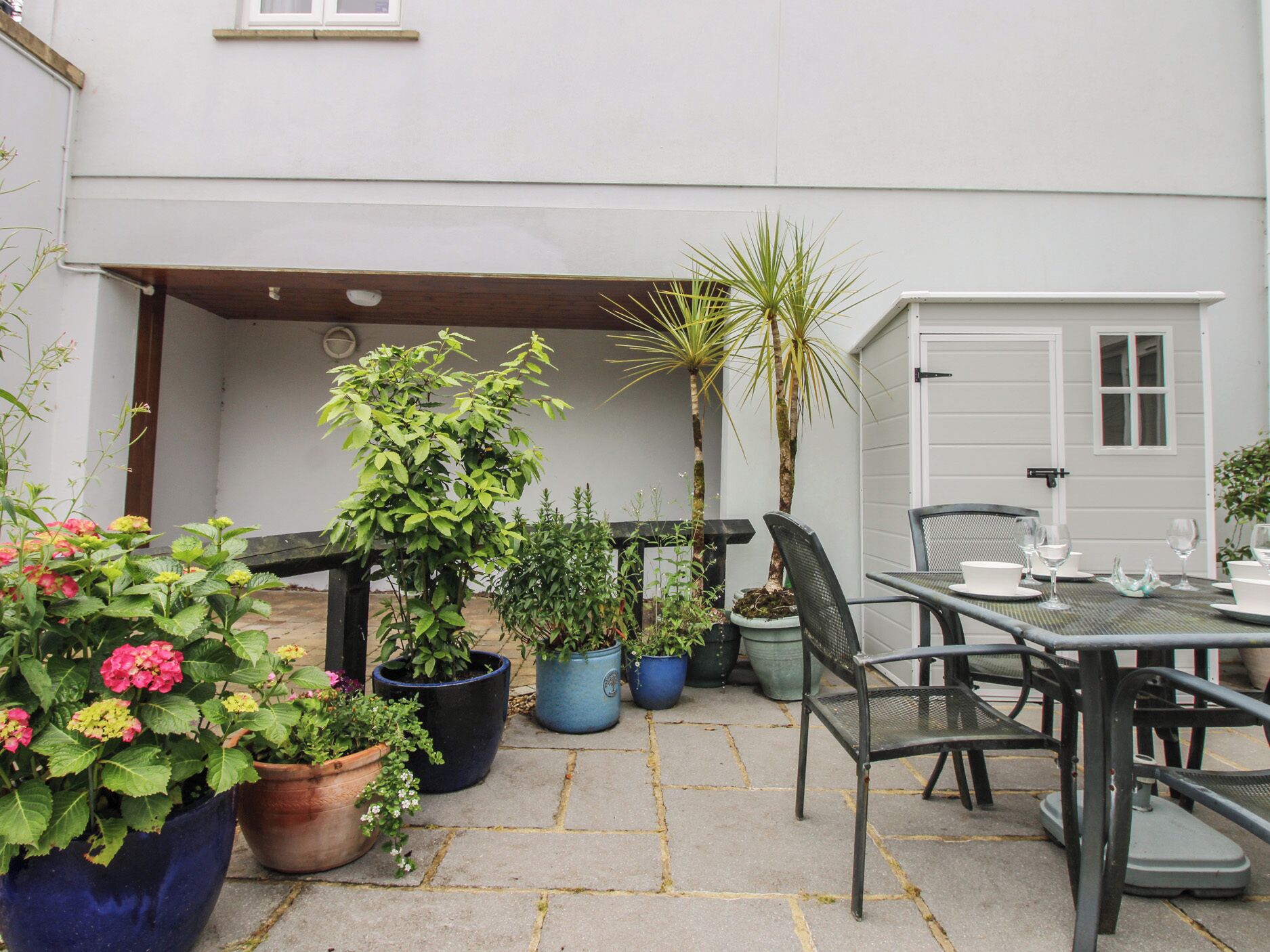 An outdoor patio with a table and chairs, surrounded by potted plants and a door to a garage.
