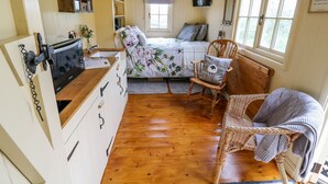 A cozy room with a bed, a wooden chair, a wicker chair, and a small kitchenette.