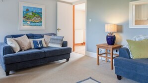 A living room with a blue sofa, a small table with a lamp, a framed picture on the wall, and a door leading to another room.