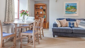 A dining area with a wooden table and chairs, a bookshelf, and a blue sofa with decorative pillows.