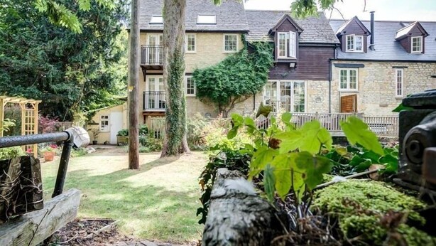 Een traditioneel stenen huis met een tuin, een houten omheining en een stenen muur.