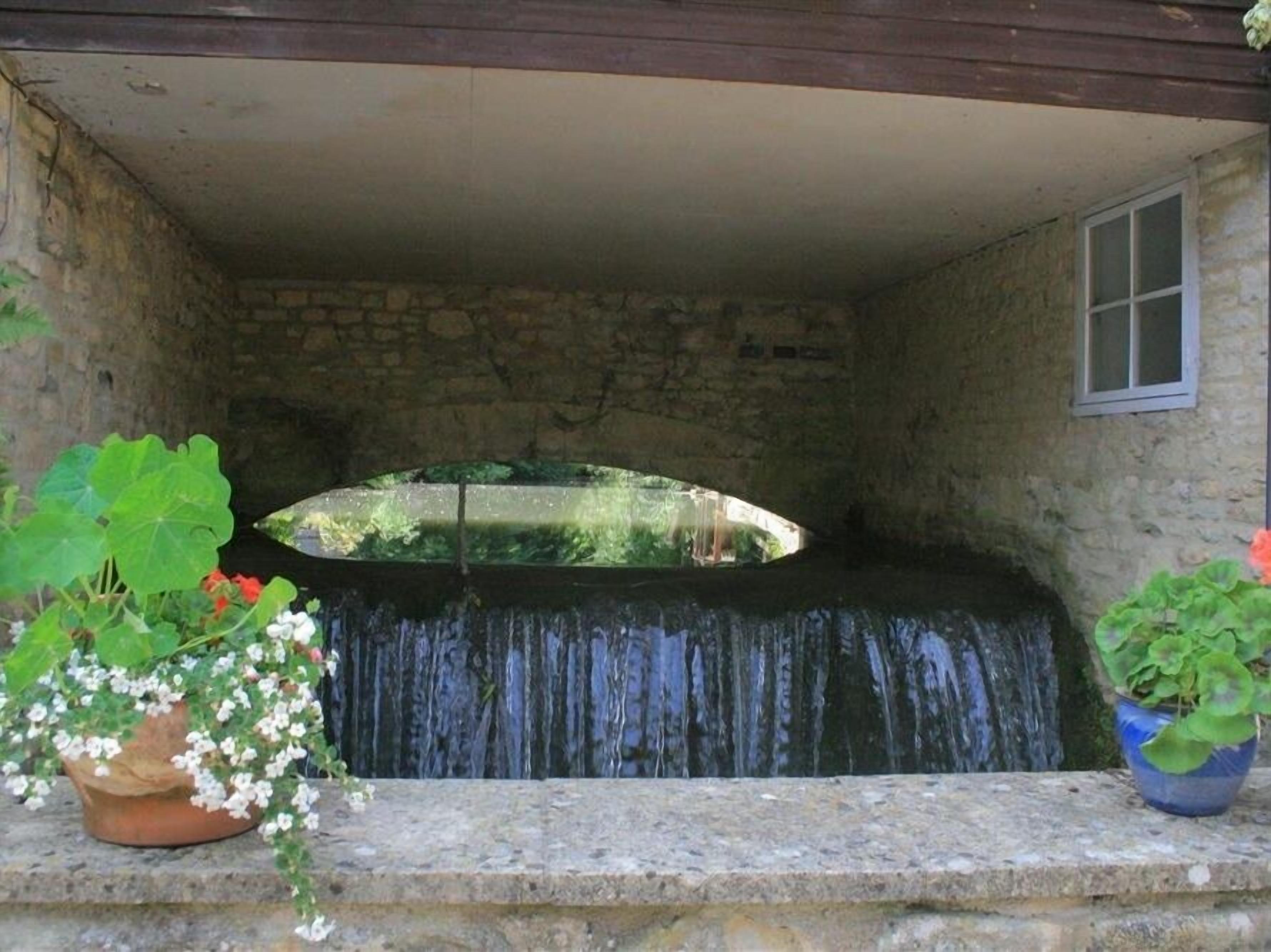 Habitación de paredes de piedra con una pequeña cascada y una ventana.
