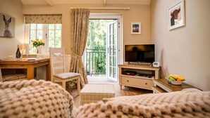 Een knus ingerichte kamer met een houten bureau, een televisie en een balkon met gordijnen.
