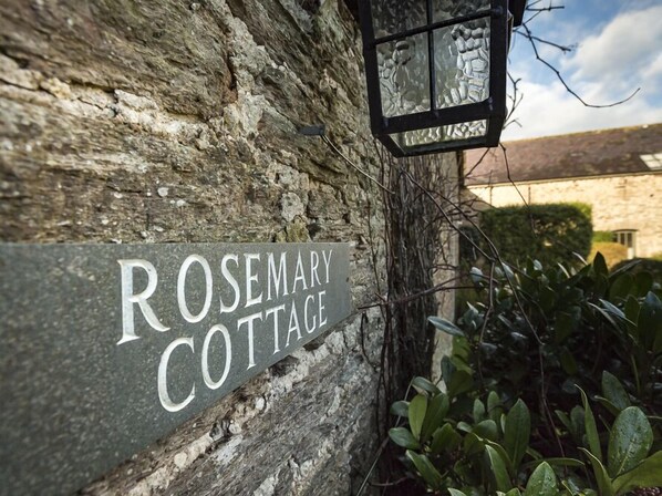 Een rustieke stenen muur met een bord waarop staat: ‘ROSEMARY COTTAGE’.