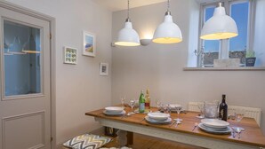 A dining area with a wooden table set for four, white pendant lights, and a window with a view. - Rosemary Cottage (Kingsbridge)