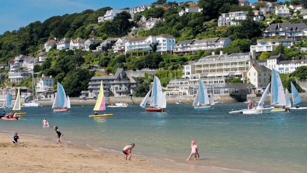 A coastal scene with sailboats on the water, a sandy beach, and houses on a hillside in the background. - Rosemary Cottage (Kingsbridge)