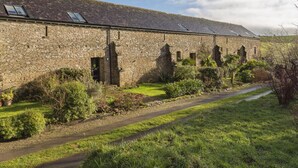 A stone building with a long corridor, small windows, and a pathway leading to it. - Rosemary Cottage (Kingsbridge)