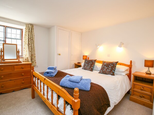 A bedroom with a wooden bed, white walls, a dresser, and a window with curtains.