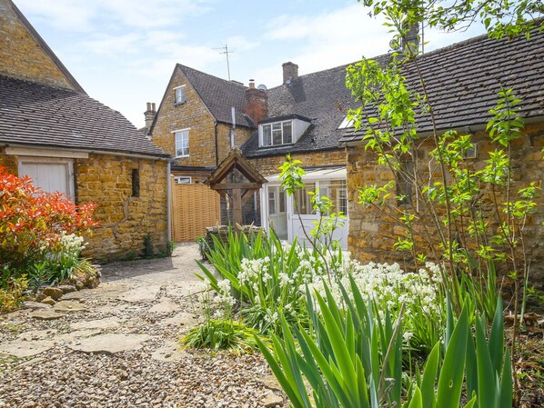 A stone building with a tiled roof, a wooden gate, and a gravel pathway leading to a white door.