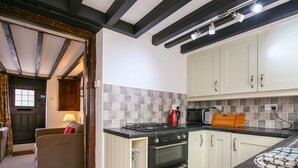 Cocina compacta con estufa a gas, horno y microondas, armarios blancos y salpicadero de azulejos.