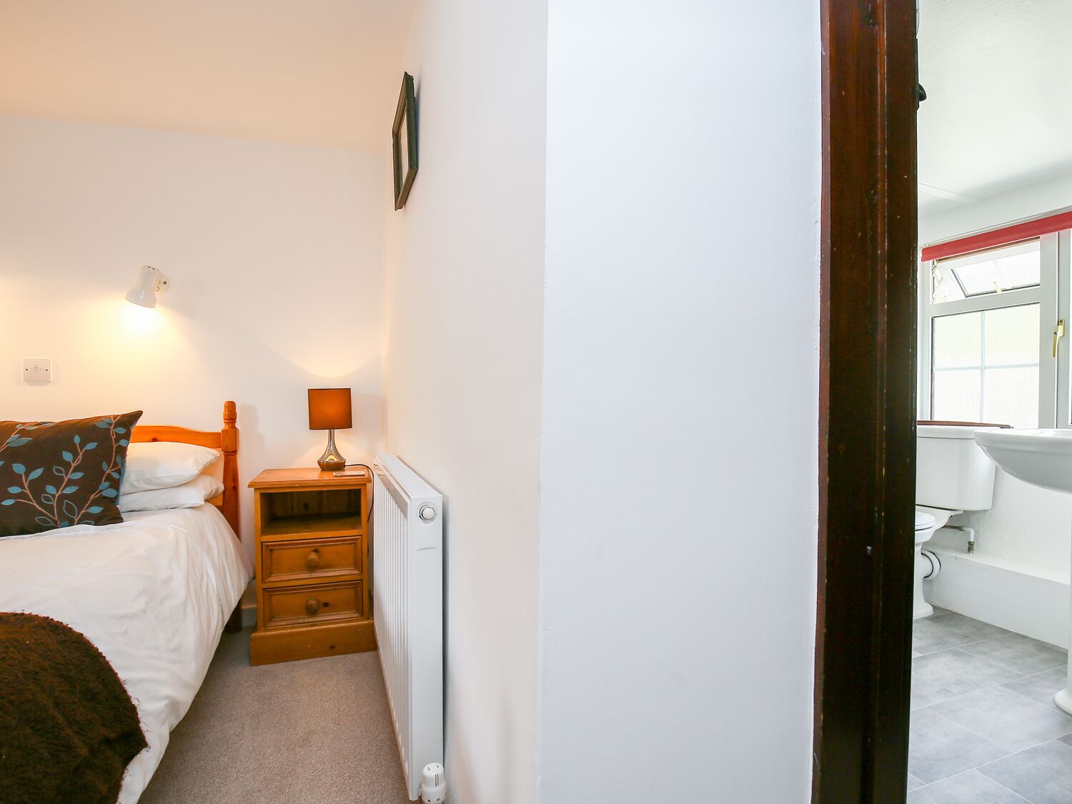 A bedroom with a bed, bedside lamp, dresser, and radiator.