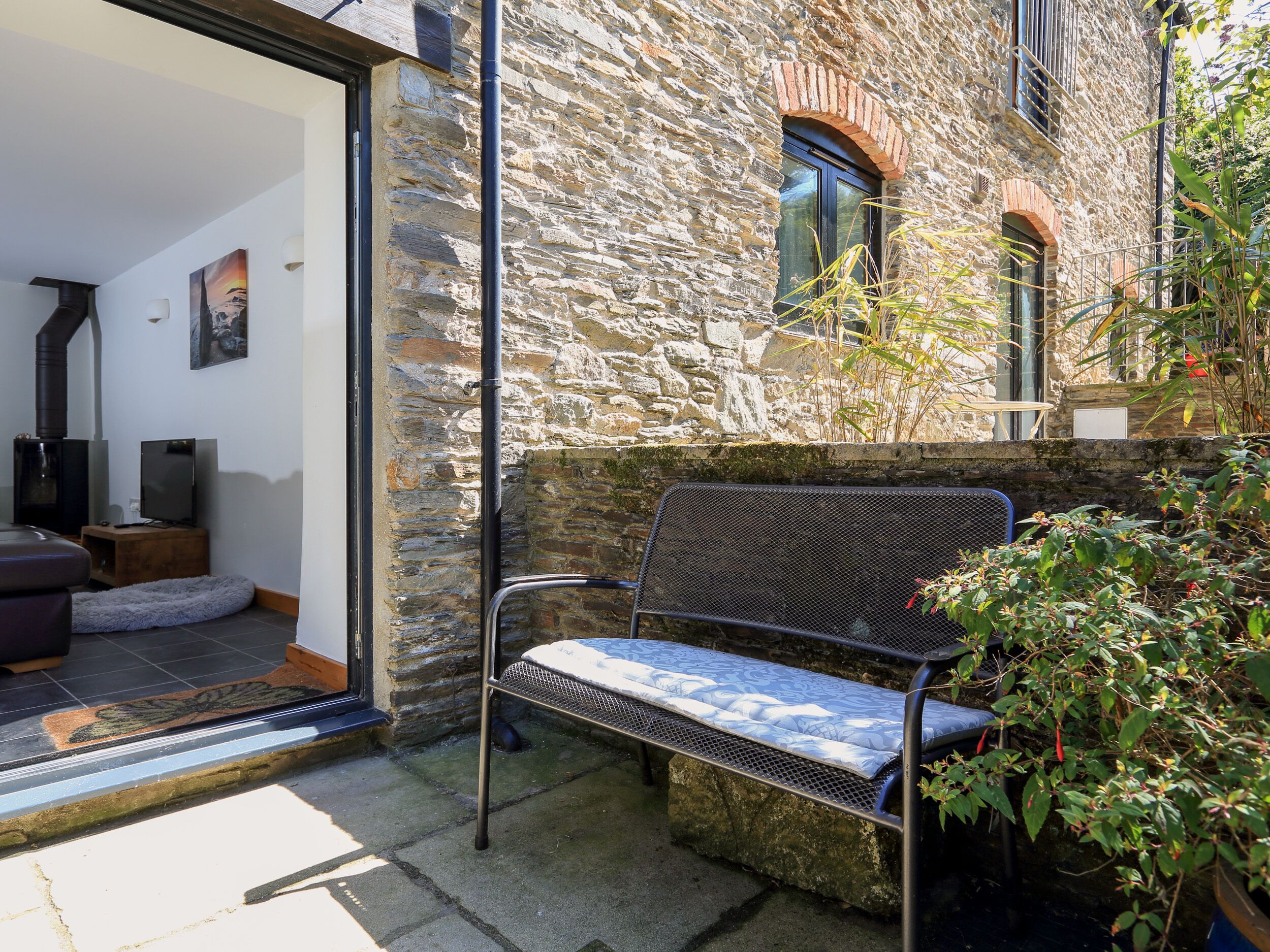 A stone building with a metal bench and a door leading to a room with a fireplace and a television.