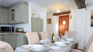 A dining area with a long table set for six, equipped with plates, glasses, and cutlery. There are two chairs, a microwave, and a toaster on the counter. - Cowslip Cottage (Kingsbridge)