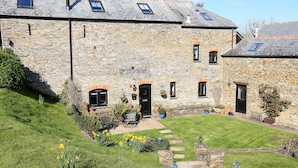 A stone building with multiple windows and doors, a small garden with stepping stones, and a grassy lawn. - Cowslip Cottage (Kingsbridge)