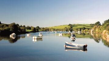 A calm river with several boats anchored, surrounded by green hills and a clear sky.