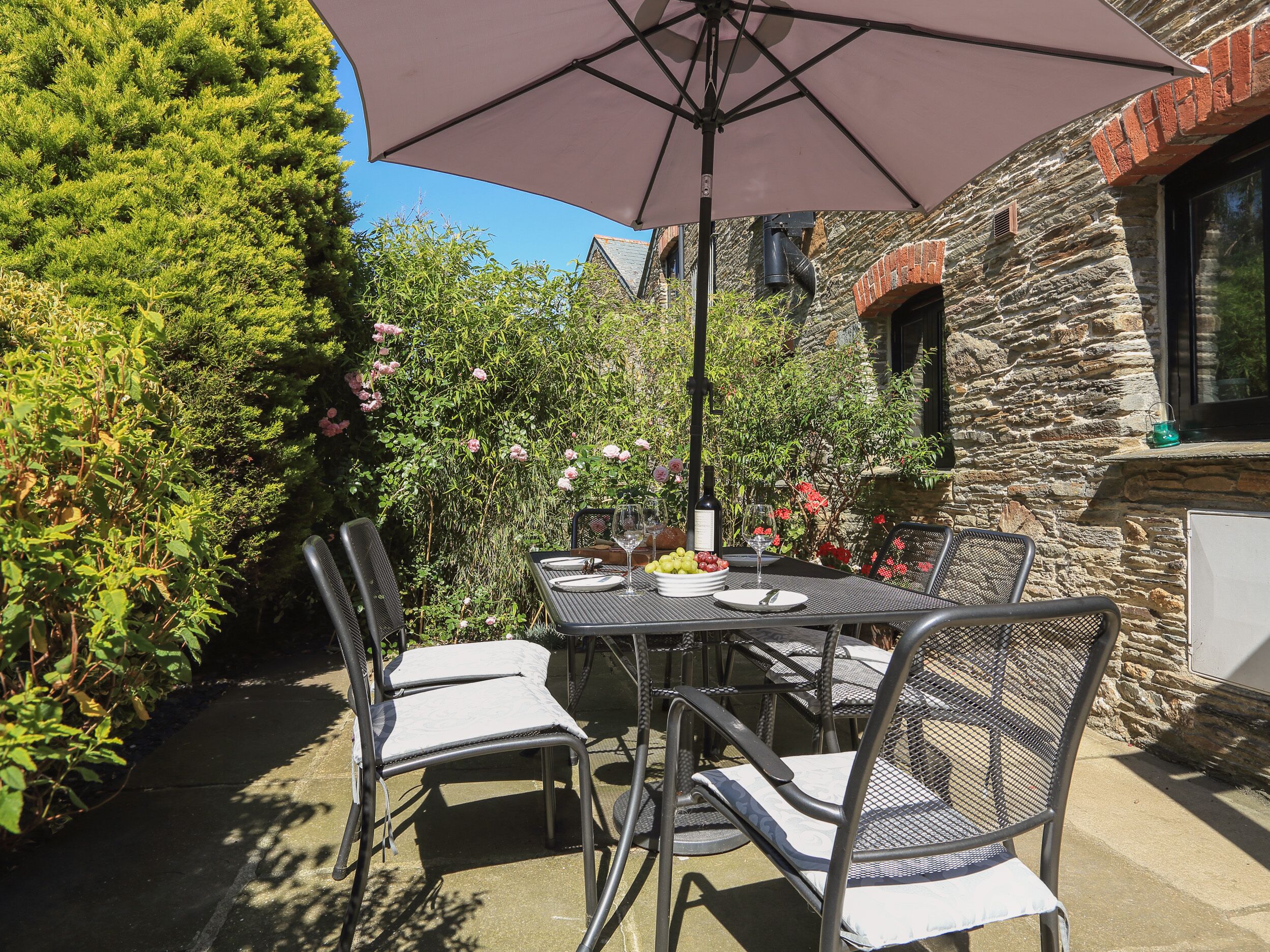 An outdoor patio with a table set for two, surrounded by chairs, under a large umbrella.