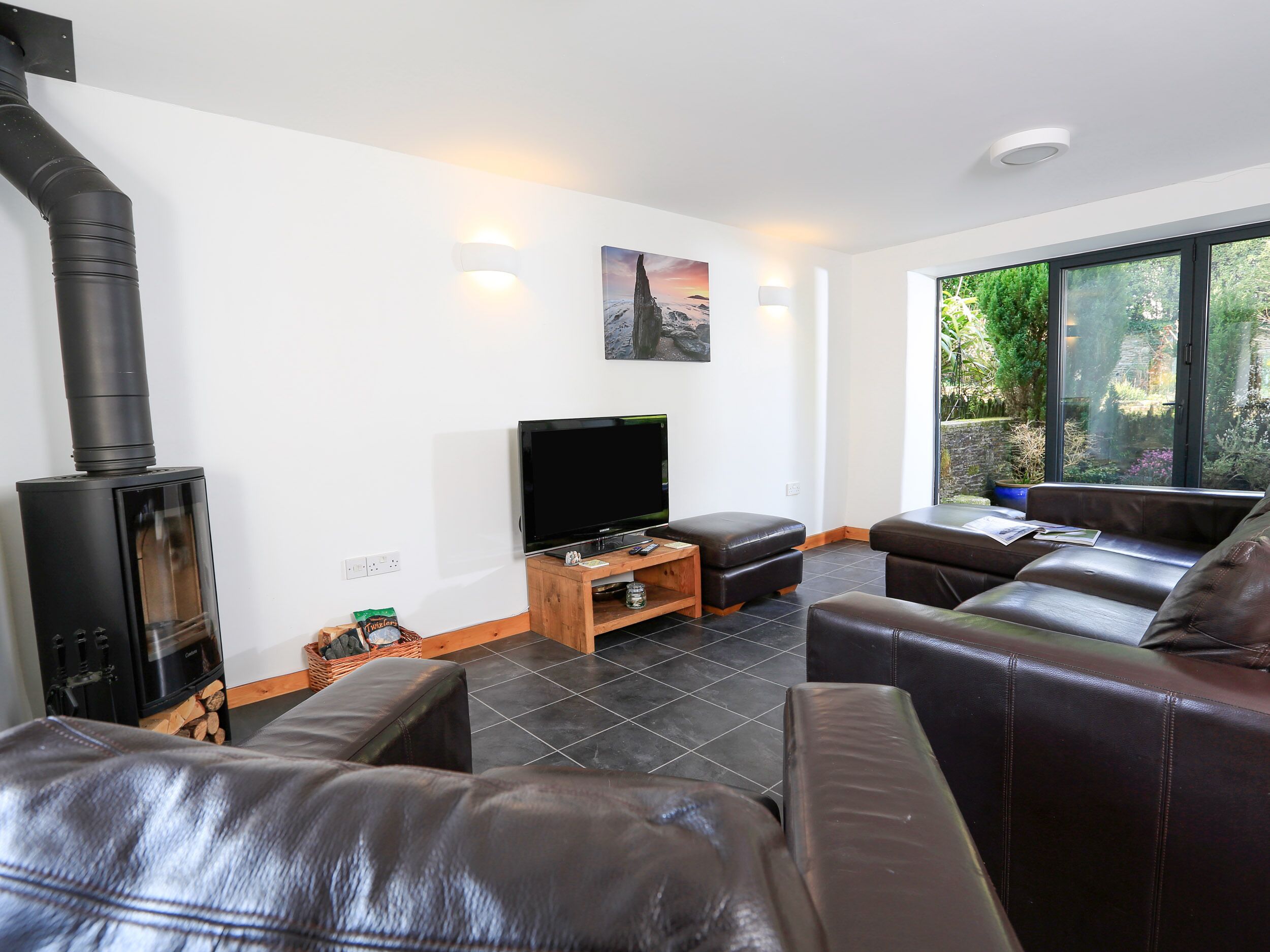 A modern living room with a fireplace, leather sofa, and a large window offering a view of greenery.