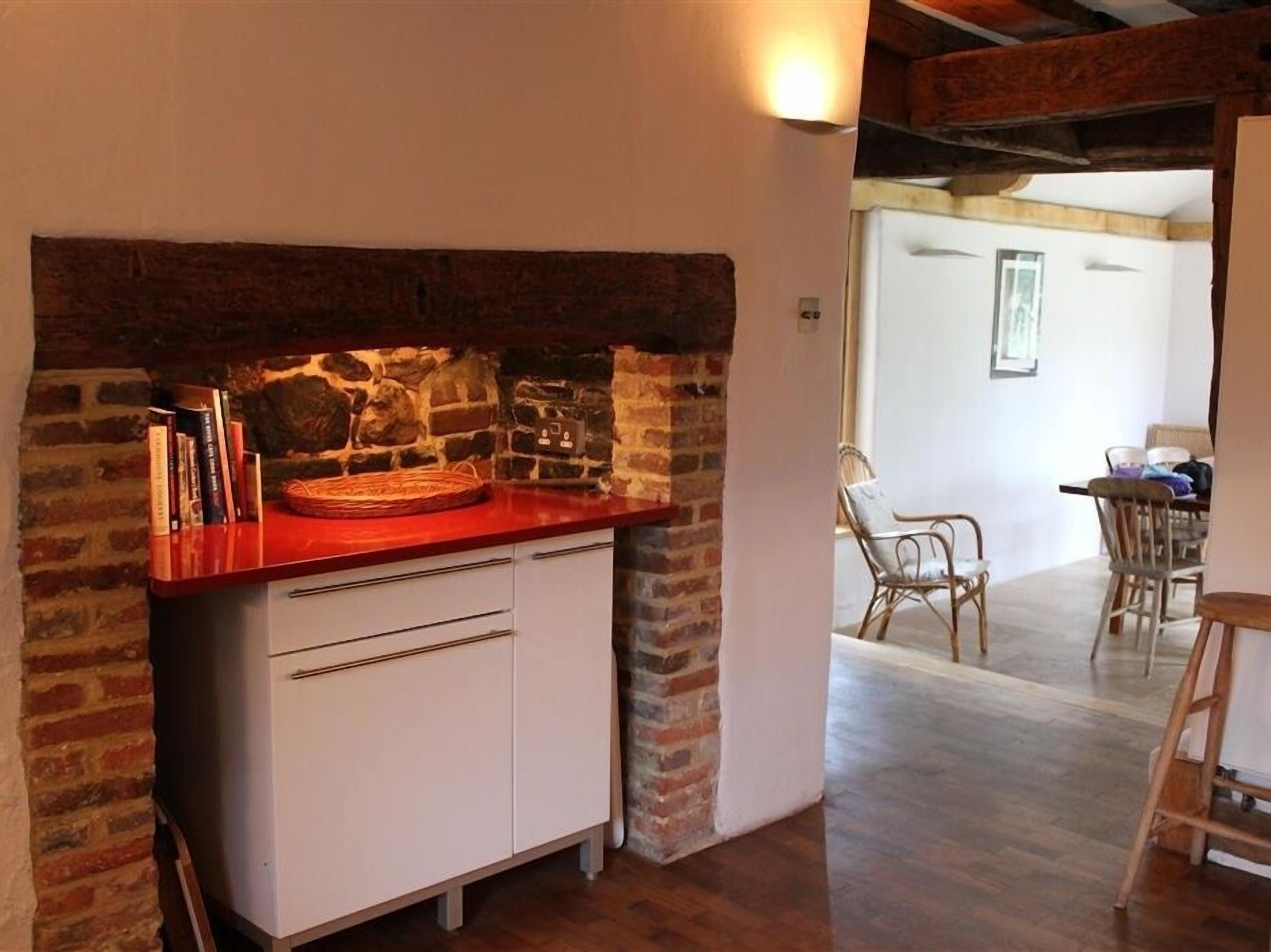 A kitchen with a brick wall, a red countertop, and a white cabinet.