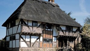 A traditional half-timbered house with a thatched roof and stone foundation.