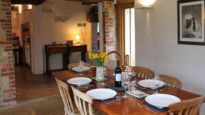 A dining area with a wooden table set for four, a vase with flowers, and a wine bottle.