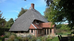 A thatched-roof house with a brick exterior, surrounded by a well-maintained garden.