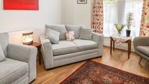 A living room with a grey sofa, two armchairs, a patterned rug, and a table with a potted plant. - The Haven (Buxton)